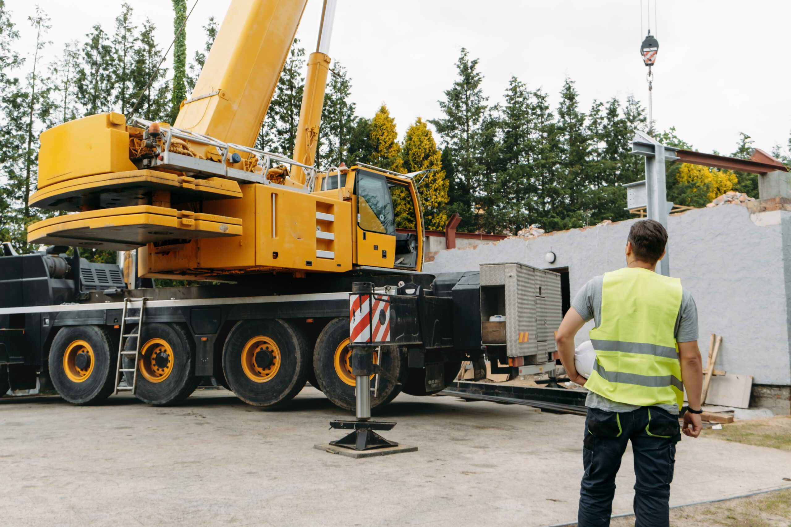 Person in a safety vest observing a 30-ton boom truck at a construction site, highlighting its operational efficiency and versatility for lifting tasks.