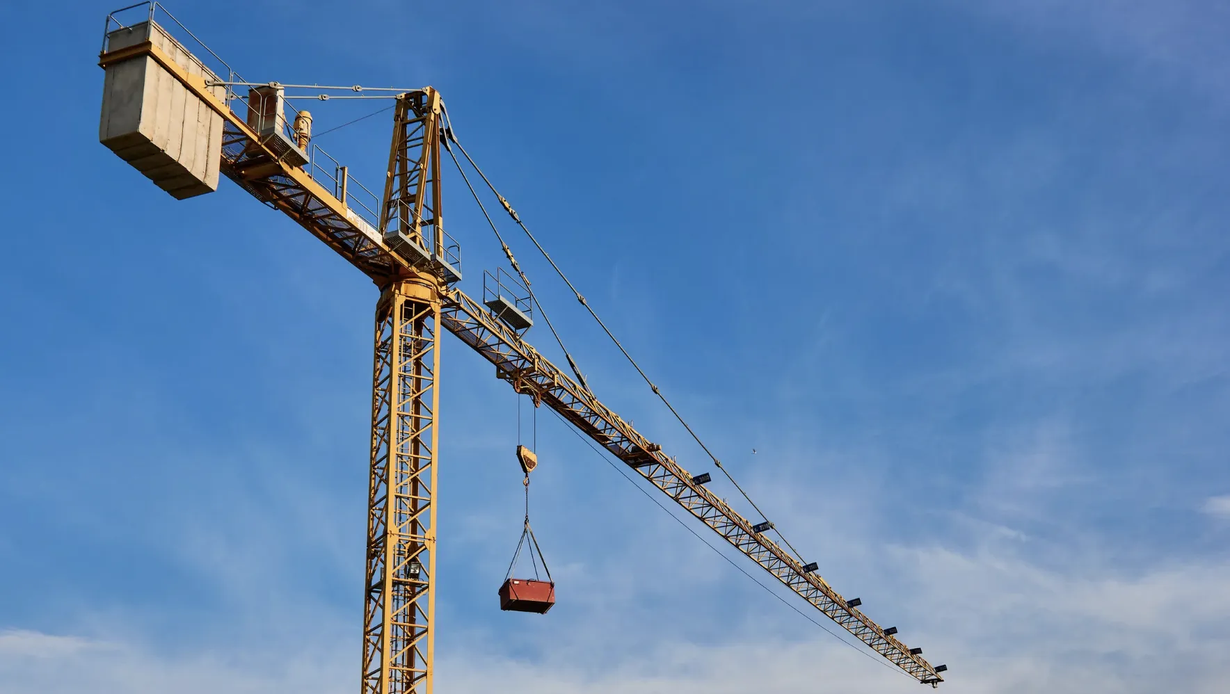 Crane lifting materials against a clear blue sky, showcasing mobility and lift capacity essential for construction projects in Massachusetts.
