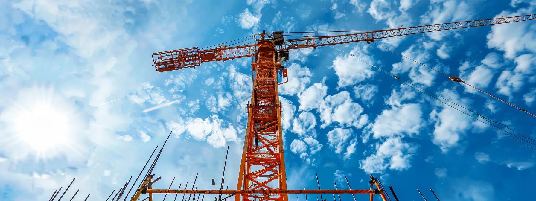 Crane towering against a bright blue sky with clouds, showcasing modern construction equipment relevant to crane rental services in Boston.