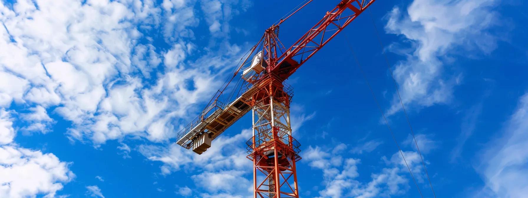 Red and white construction crane against a blue sky with clouds, representing crane rental services in Boston and key considerations for project managers.