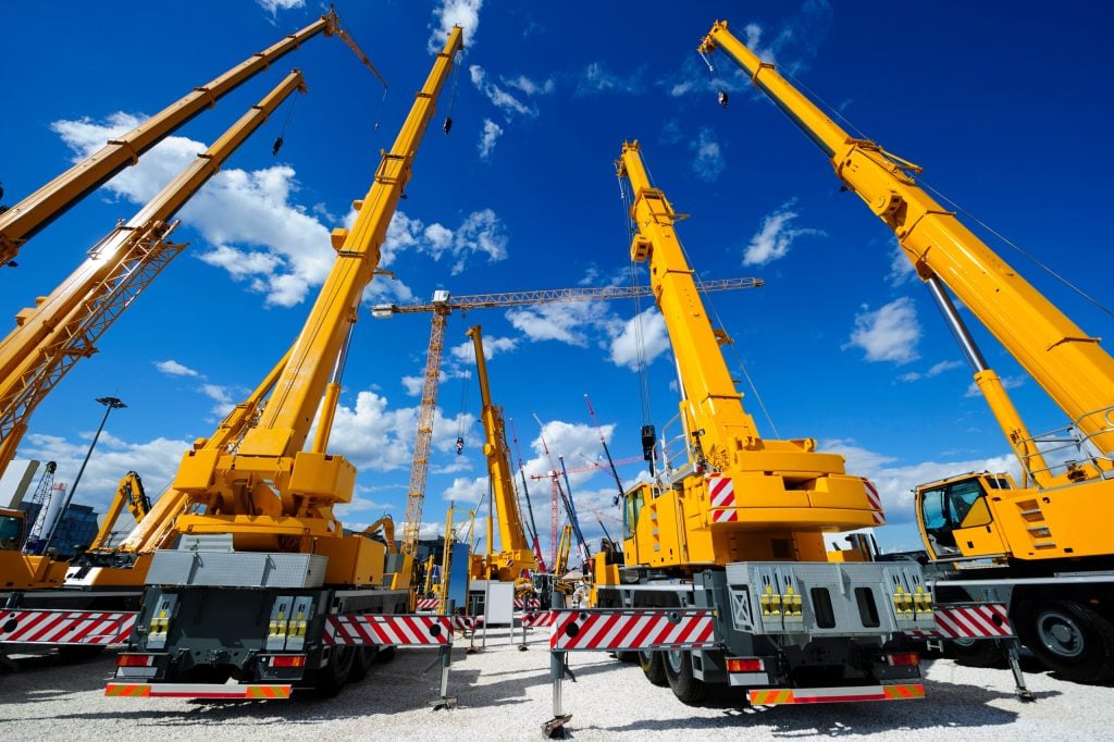 Yellow cranes and construction equipment against a blue sky, showcasing heavy lifting machinery for crane rental services in Southern Massachusetts.
