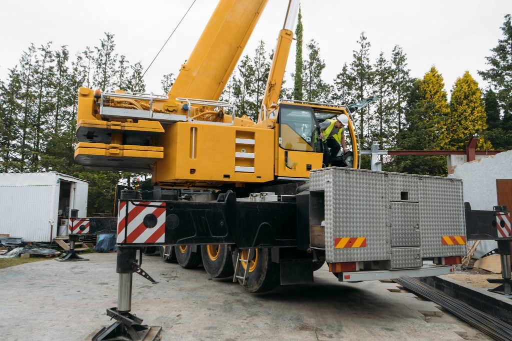 Crane operator in yellow safety gear operating a mobile crane on a construction site in Northern Massachusetts, emphasizing professional crane rental services and safety.