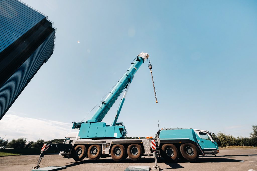 Blue crane lifting mechanism with extended arm and hooks, positioned near a building, emphasizing precision lifting for construction and HVAC projects in Foxborough, MA.