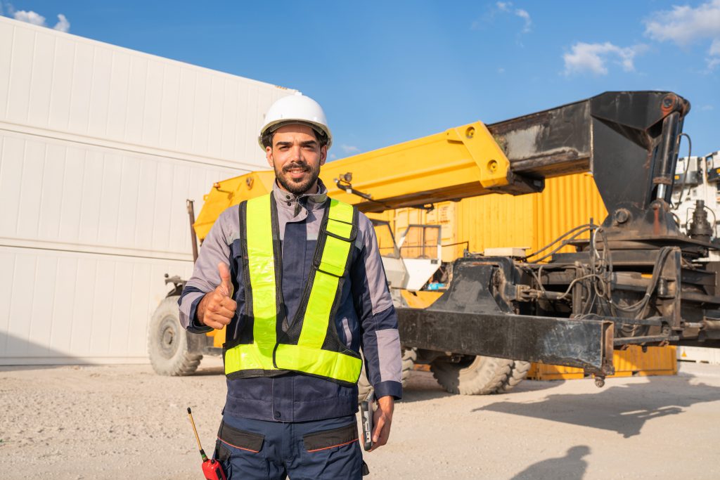 Container yard worker in safety gear giving a thumbs-up, with crane equipment and containers in the background, emphasizing professional crane operation and safety in Bridgewater, MA.