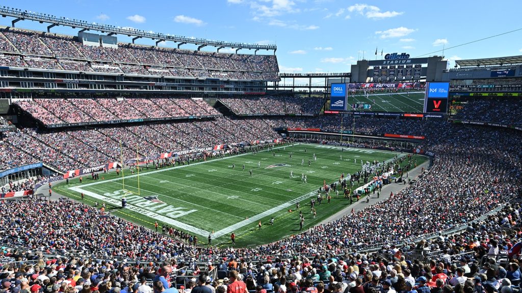 Crowd at Gillette Stadium during a football game, showcasing the field, goalposts, and large scoreboard, highlighting Foxborough's vibrant sports culture.